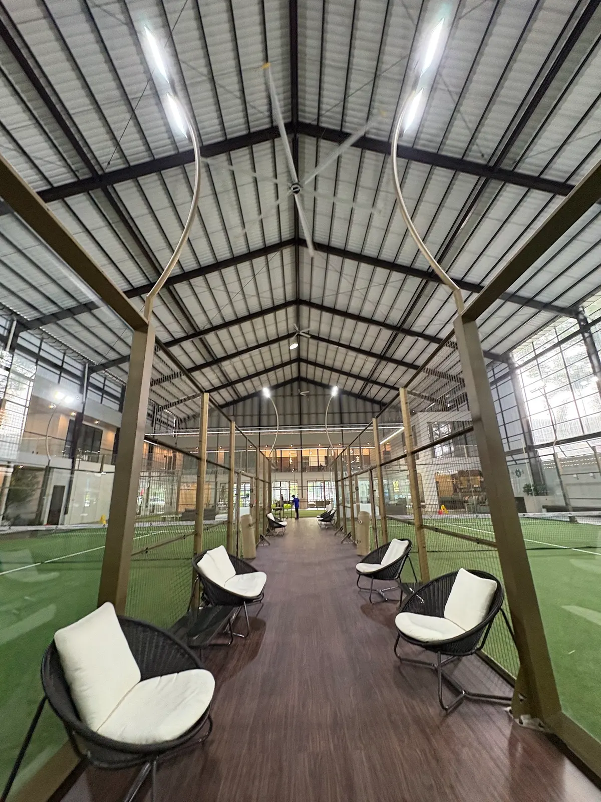 Boardwalk with white lounge chairs running between the glass padel courts